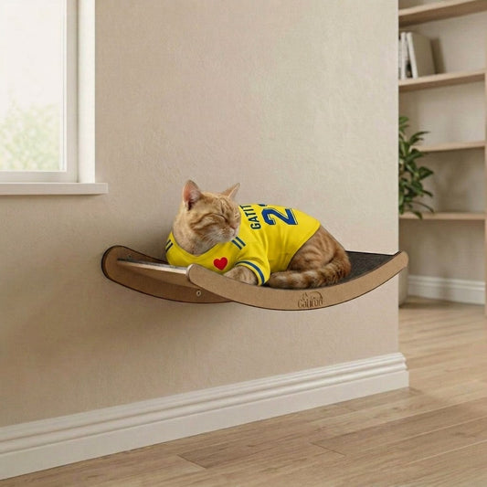Cama de pared para gatos Gatitud LUNA mediana, de madera MDF, con borde contenedor y tela gris. Gato naranja con camiseta amarilla duerme.