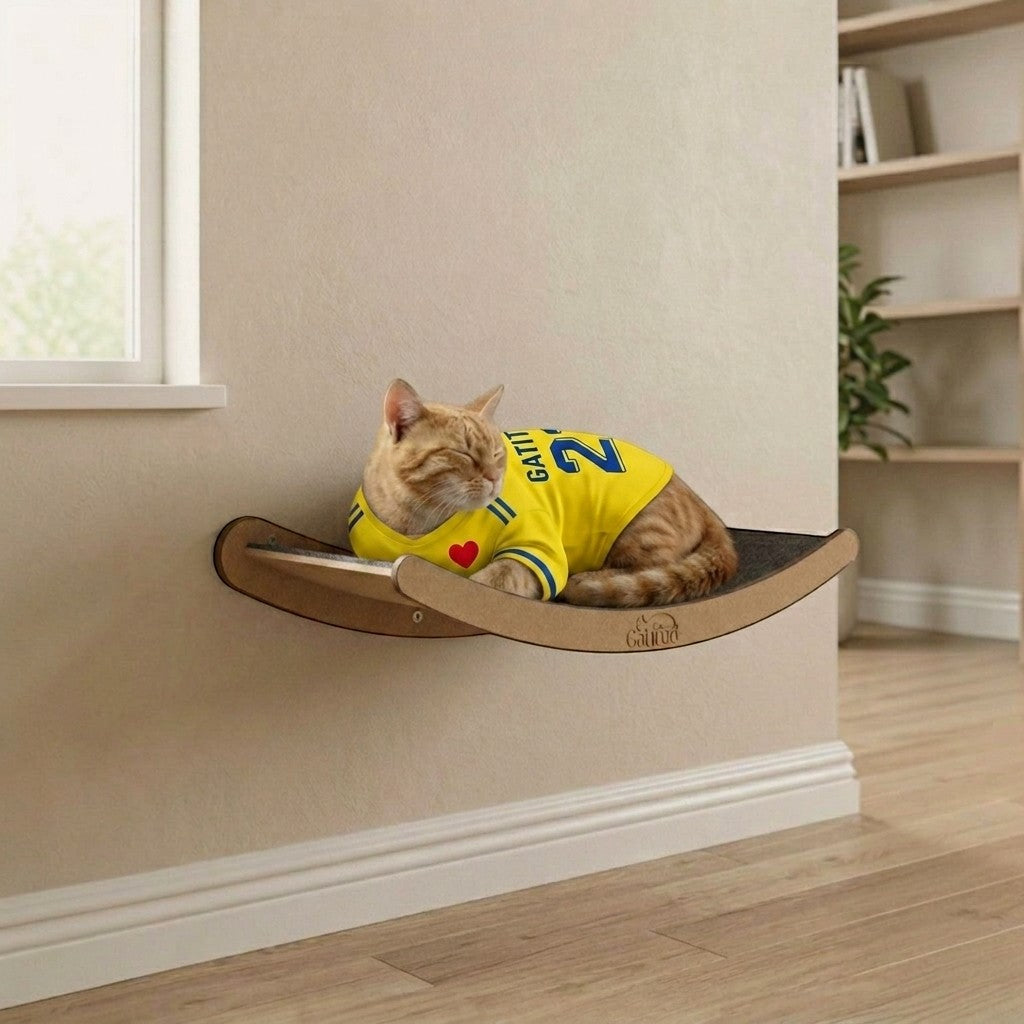 Cama de pared para gatos Gatitud LUNA mediana, de madera MDF, con borde contenedor y tela gris. Gato naranja con camiseta amarilla duerme.