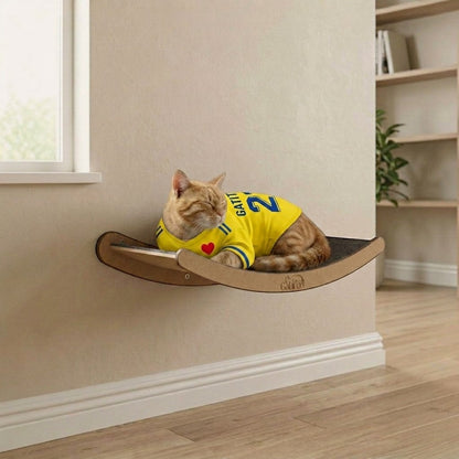 Cama de pared para gatos Gatitud LUNA mediana, de madera MDF, con borde contenedor y tela gris. Gato naranja con camiseta amarilla duerme.