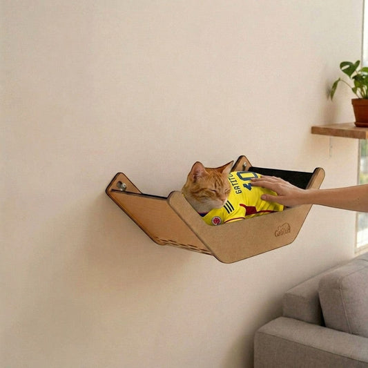 Cama V Hamaca de Gatitud Store en madera MDF con gato naranja durmiendo, fijada a la pared para uso felino.