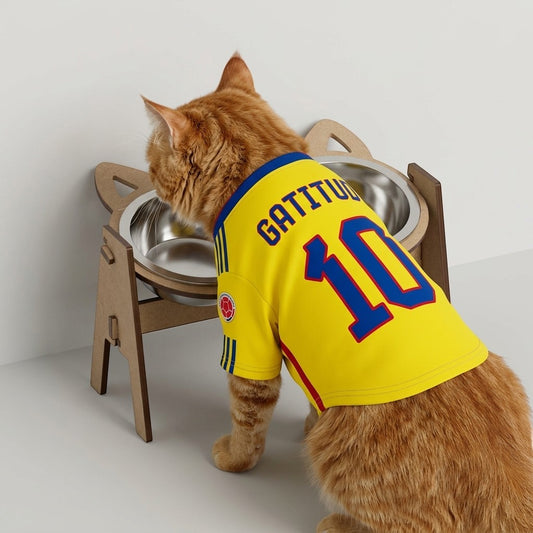 Gato naranja con camiseta de fútbol comiendo en comedero elevado doble de madera MDF de Gatitud Store